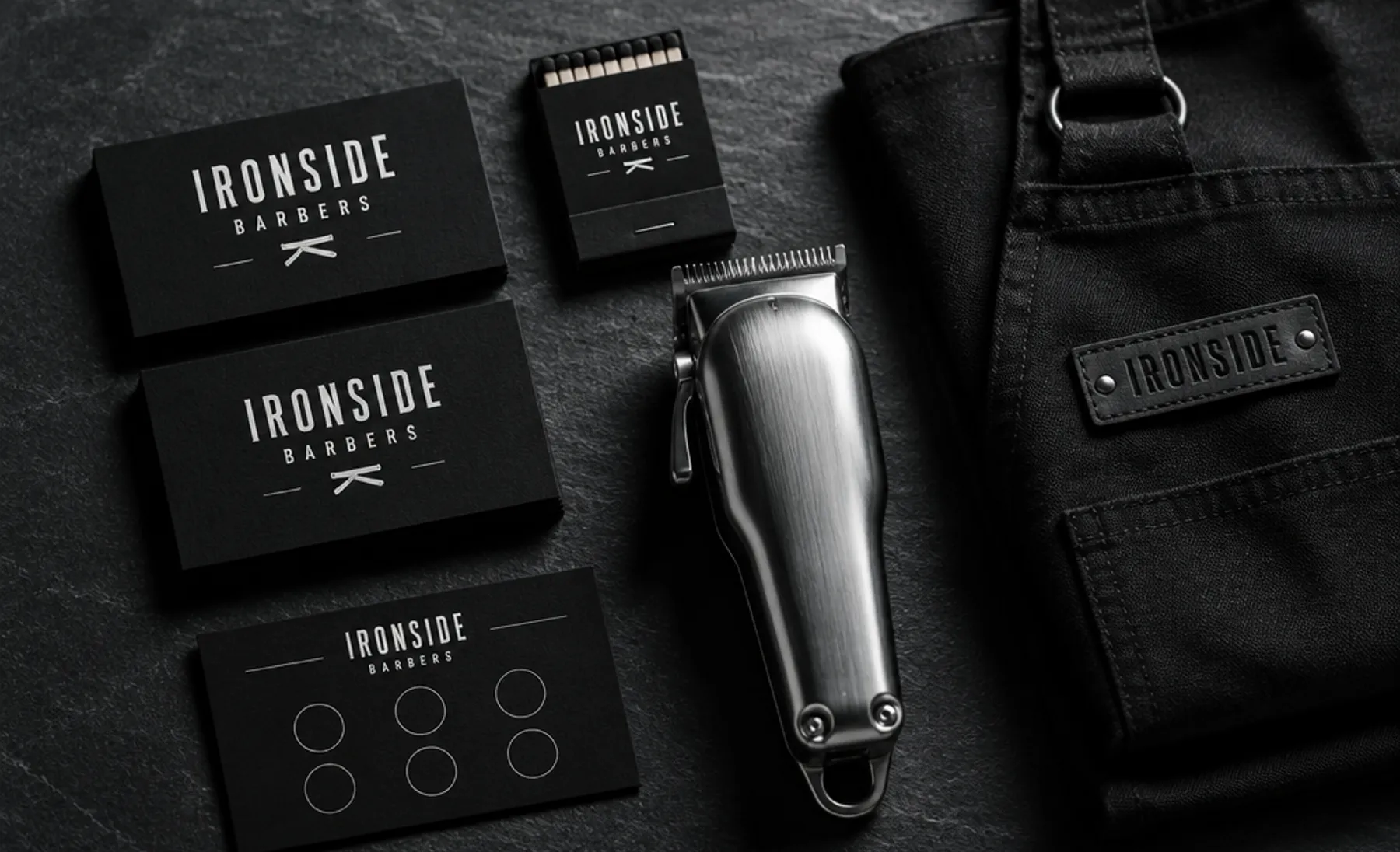 Example branding for an invented barber shop, Ironside Barbers: matte black business cards with a condensed wordmark and razor mark, a matchbook, an apron tag and a loyalty stamp card